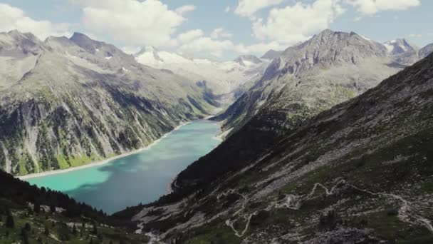 遠くに氷河と美しい高山山脈の風景 山の谷の大きなシュレージス貯水池バリア湖 晴れた日に小さなハイキングコースを後方に明らかにする飛行 — ストック動画