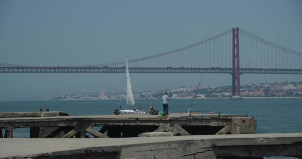 葡萄牙里斯本一个码头的老渔夫25 Abril桥和帆船在远方 — 图库视频影像