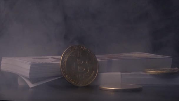 黄金比特币靠在一堆一百美元的钞票上 黑黑的背景下冒着轻烟 — 图库视频影像