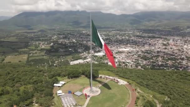 위높은 녹색의 멕시코 국기를 공중에서 회전시키는 보이는 골짜기에 도시가 보인다 — 비디오