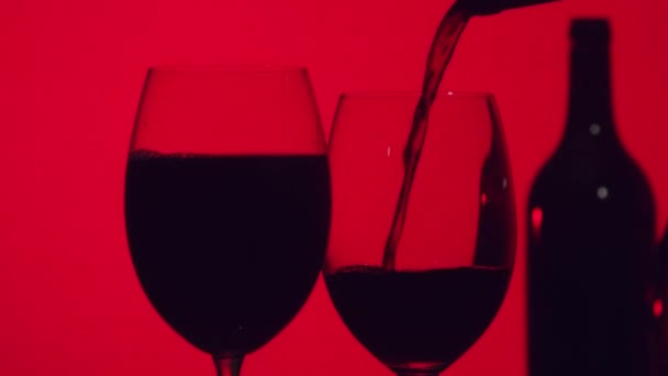 Sylwetka Kieliszka Czerwonym Winem Wylewającym Się Butelki Czerwonym Tle Zbliżenie — Wideo stockowe