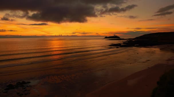 英国康沃尔 靠近圣艾夫斯的一个平静的日落黄昏海滨海滩的电影图像无缝视频循环 红色和橙色的天空 柔和的海浪和灯塔 开阔的全景 浪漫的旅游 — 图库视频影像