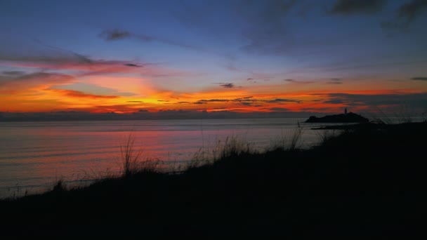 イギリスのコーンウォールにあるSt Ivesに近い日没の夜の海辺のビーチのシームレスなビデオループを撮影します 赤とオレンジの空 柔らかい波と灯台 広いパノラマビュー ロマンチックな観光 — ストック動画