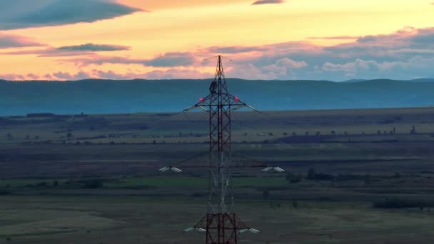日没の丘の前の田園地帯に電気パイロンを示す空中ビュー — ストック動画