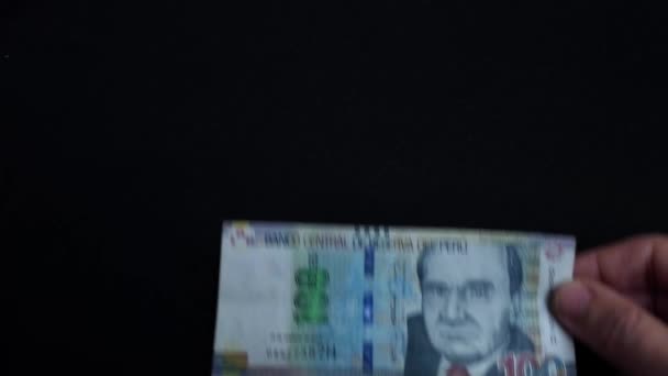 黒い背景の前でお金を保持する手のビデオ ペルーの通貨であるペルーソール100枚の紙幣 — ストック動画