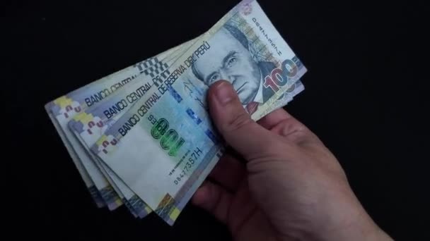 4K视频中的一只手拿着许多纸钞 秘鲁索尔是秘鲁的国家货币 手拿着 摊开钞票 旋转着 向两边展示 前面是黑色的背景 — 图库视频影像
