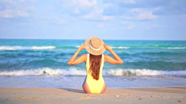 水着姿のロンリーウーマンのバックビュー熱帯海の目の前のビーチに座って腕を上げる喜びに満ち スローモーション — ストック動画