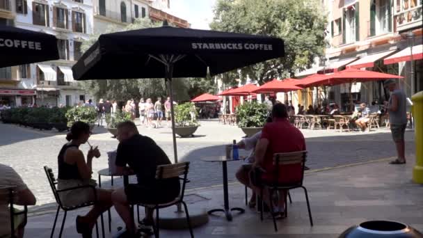 コーヒーを飲む人でいっぱいのスターバックスコーヒーテラス スターバックスで傘の下に座って一日を楽しむ人 — ストック動画