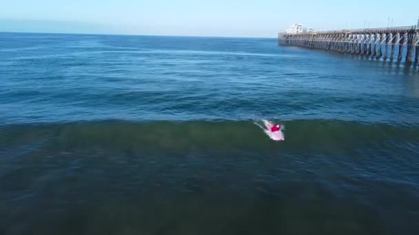 海側の桟橋でピンクのロングボードサーフィンをしているサーファーは — ストック動画