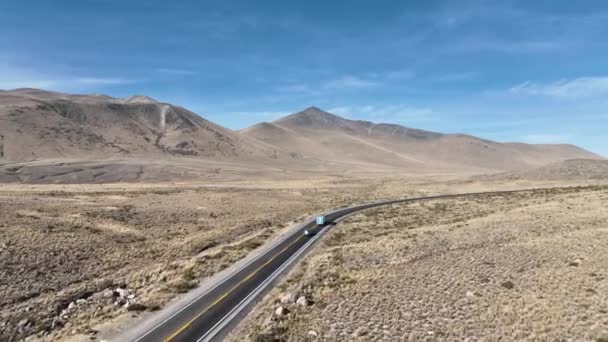 南米ペルーのアンデス山脈の湾曲した山で重い荷積みトラックの後ろに乗っている車のドローンショットに従ってください — ストック動画