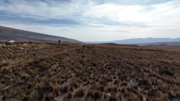 无人机在秘鲁公路旁边干枯的草地上盘旋 重型车辆从右到左经过 — 图库视频影像