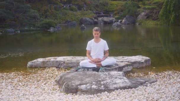 Praktik Laki Laki Kaukasia Putih Meditasi Duduk Batu Oleh Kolam — Stok Video