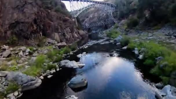 Fpvドローンは 米国カリフォルニア州の鉄道橋と岩の多いフェザー川の上で低ショット — ストック動画