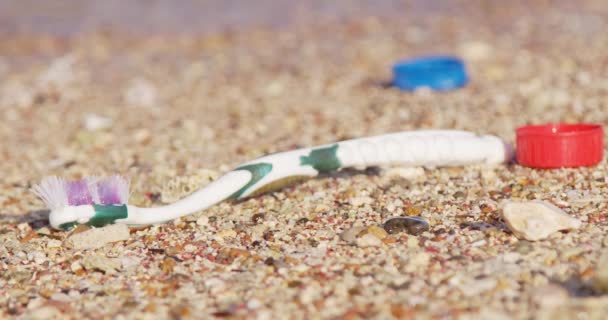 旧的塑料牙刷和瓶盖被冲刷到沙滩上 被水流冲走 海浪冲走 — 图库视频影像