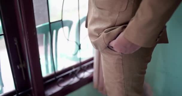ビジネスマンの体の詳細 緑の背景にズボンのポケットに男の手を閉じます ベージュのジャケットと白いシャツを着た男 窓のそばに立つ — ストック動画