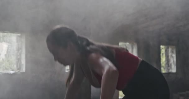 一名身穿健美服装的年轻女子在一家老旧的工业大厅进行体育锻炼 将一名铁路熟睡者扶起来 — 图库视频影像