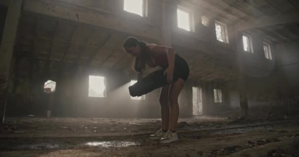 一名身穿健美服装的年轻女子在一个古老的工业大厅里进行体育锻炼 将一名铁路熟睡者扶起来 低角度宽射门 — 图库视频影像