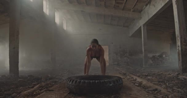 在一个废弃的老工业大厅里 一个穿着大轮胎的年轻女子在一个储气罐顶部操练 — 图库视频影像
