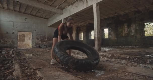 一个年轻的女人在一个工业大厅里带着一个大轮胎锻炼 — 图库视频影像