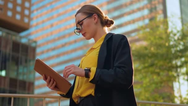 女性弁護士が屋外のバルコニーにデジタルタブレットPcで立っている夕日と高層ビルに触れるメガネフレーム — ストック動画