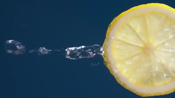 青黒地にレモンスライスから流れる水のスローモーションマクロショットの垂直 — ストック動画