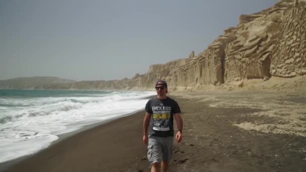 Один Чоловік Сонцезахисних Окулярах Ходить Босоніж Пляжі Влчада Санторіні Греція — стокове відео