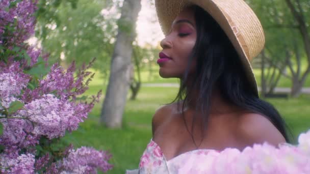 Black Woman Summer Dress Straw Hat Smells Pink Lilac Flowers — Vídeos de Stock
