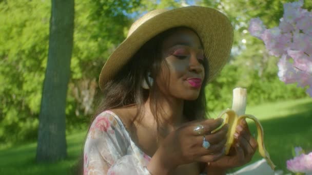 Африканская Женщина Носит Шляпу Платье Парке Пикник Ест Банан Смотреть — стоковое видео