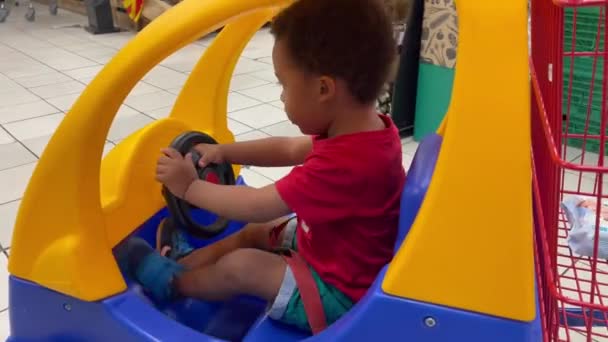 Szczęśliwy Dwuletni Czarny Dzieciak Jeżdżący Plastikowym Samochodzikiem Supermarkecie Pomagający Mamie — Wideo stockowe
