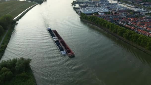 川の右側にあるスライドレヒトのベネデン マーウェドと都市部の不動産住宅街を航行する2つの大きな内陸アメウラス船のトップダウンの空中撮影 — ストック動画
