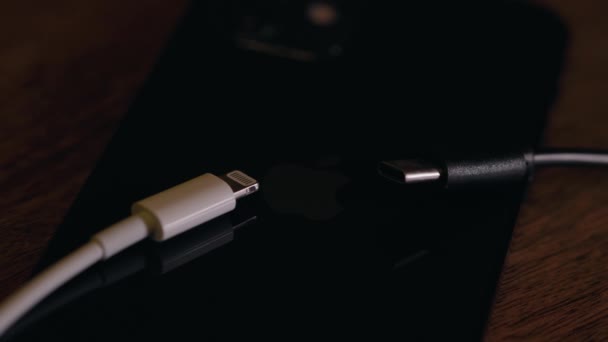 机の上にアップルのIphoneの携帯電話の背面に置かれた異なる充電ケーブル — ストック動画