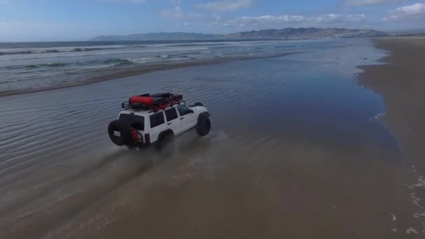 Een Witte Jeep Cherokee Rijdt Noordwaarts Het Strand Door Golven — Stockvideo