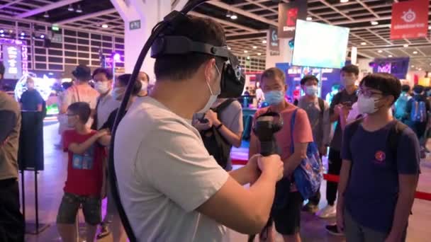 中国のゲーマーは 訪問者が香港で開催された香港コンピュータ通信フェスティバルで彼がプレイするのを見ると 仮想現実 マルチプレイヤーシューティングゲームをプレイします — ストック動画