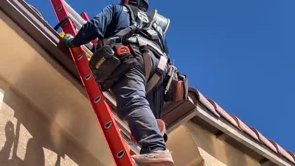 ソーラーパネル設置技術者は 屋根を身に着けているツールと安全ハーネスにアクセスするためにはしごを登る — ストック動画