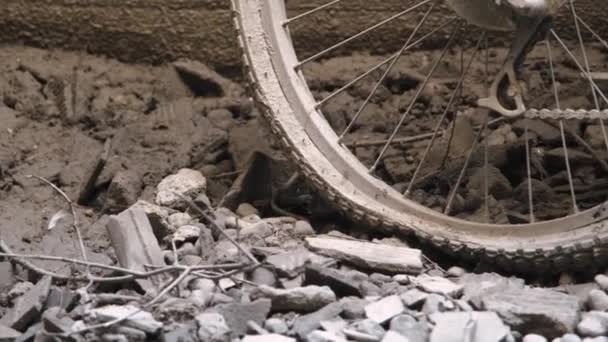 瓦礫に覆われた地面の上に砂の壁にもたれて左の平らなタイヤを持つ放棄された自転車は 汚れで覆われています — ストック動画
