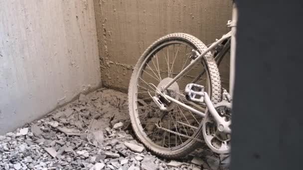 瓦礫に覆われた地面の上で土に覆われた砂の壁にもたれて左の平らなタイヤを持つ2台の放棄された自転車 — ストック動画