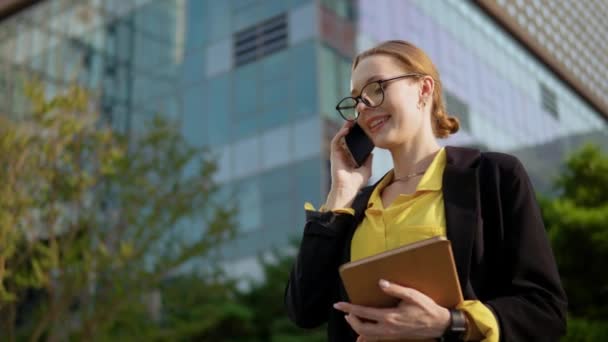 企業ビルの前でビジネスプロジェクトの屋外で電話で話す陽気なビジネスマンの女性 — ストック動画