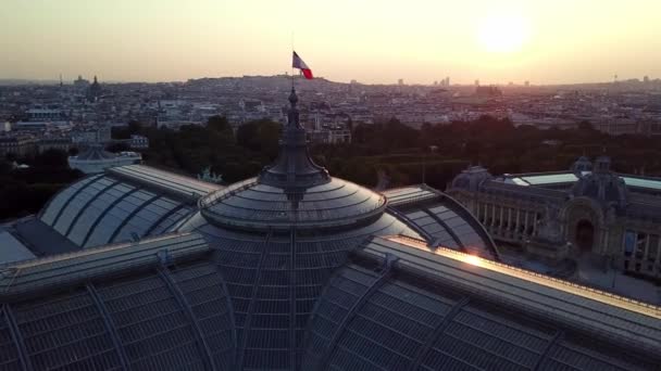 夏の黄金の日の出 パリの街の美しい景色を背景に フランスの旗が上を流れるグランド パレの壮大なガラスの屋上を周回するドローン ビュー — ストック動画