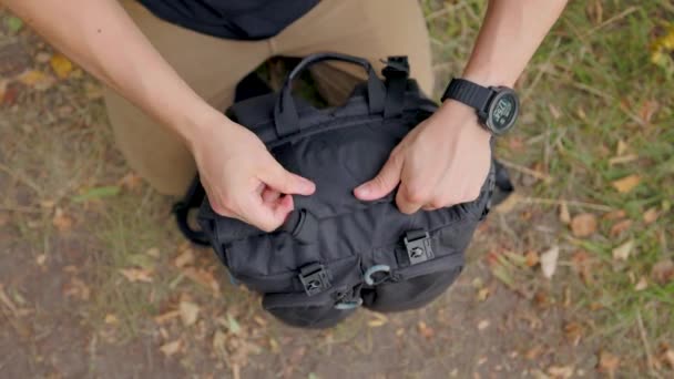 手は袋の上を丸めて閉じます 男性ハイカーは ハイキングバックパックの上にバックル付きストラップを取り付けます バッグのトップダウンビュー — ストック動画