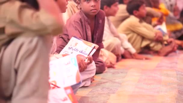 本とペンを手に持って座っている間にパキスタンで勉強している多くの十代の子供のビデオ — ストック動画