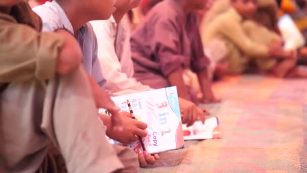 パキスタンの田舎の学校で本を手にマットの上に座っている多数の学生のビデオ — ストック動画