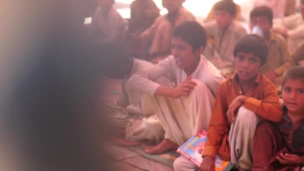 パキスタンの農村部の学校で彼らの手の本で地面にマットの上に座っている男の子の大規模なグループのビデオ — ストック動画