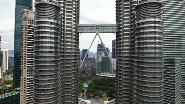 マレーシアのクアラルンプールにあるペトロナスタワー 双塔とスカイブリッジの下を飛ぶドローンの接近 — ストック動画