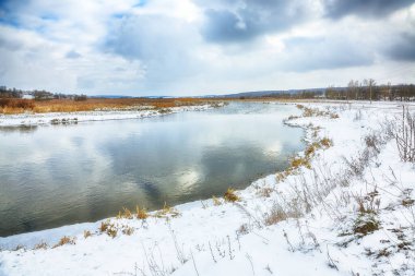 Gün batımında nehir kıyısında kış manzarası. Kar ve nehirle kaplı güzel kış manzarası