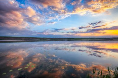 Gölün üzerinde dramatik bir gün batımı. Göldeki nilüferler. Gök ve bulutlar göle yansıyor
