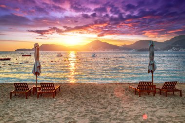 Budva yakınlarındaki Sveti Stefan 'da şezlonglar ve şemsiyelerle plajda büyüleyici bir gün batımı. Konum: Budva Riviera, Karadağ, Adriyatik denizi, Avrupa