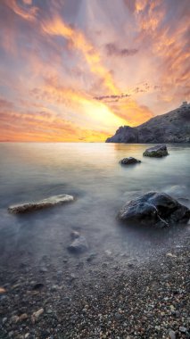 Gün batımında inanılmaz deniz manzarası. Uzun vadede güzel bir deniz manzarası. Önplanda taşlar