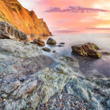 Gün batımında inanılmaz deniz manzarası. Uzun vadede güzel bir deniz manzarası. Önplanda taşlar