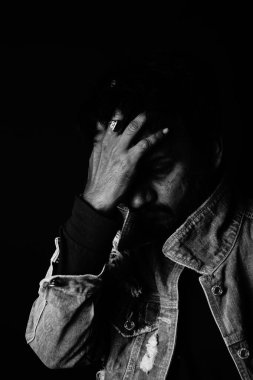 Üzgün adamın eli kafasında, elinde siyah beyaz bir fotoğrafla duruyor.