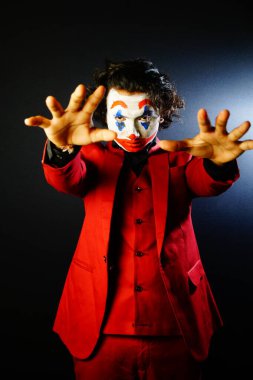 man in joker face makeup showing hands, in red formal